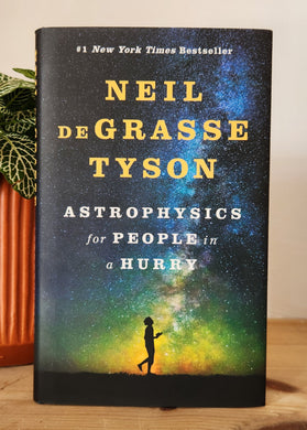 Book titled 'Astrophysics for People in a Hurry' by Neil deGrasse Tyson on a wooden surface with a plant in the background.