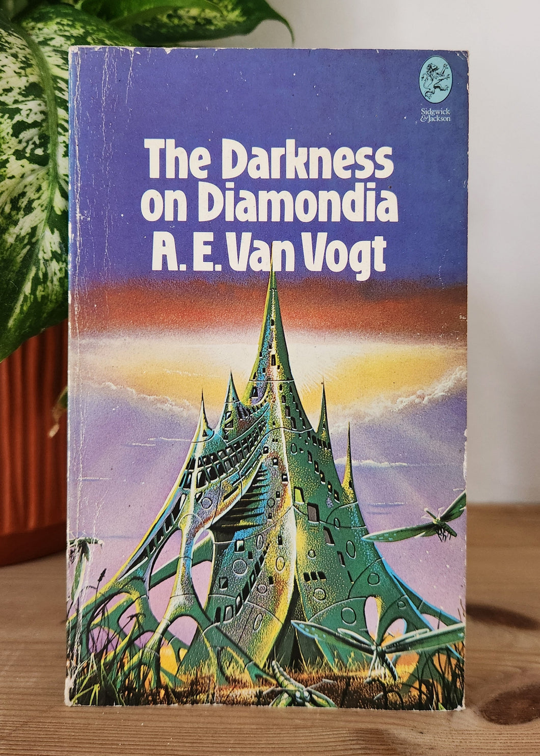 Book titled 'The Darkness on Diamondia' by A.E. Van Vogt on a wooden surface with a plant in the background