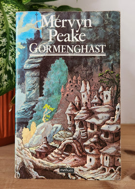 Book titled 'Gormenghast' by Mervyn Peake on a wooden surface with a plant in the background.